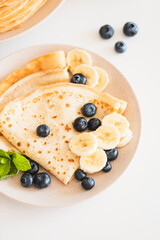 French crepes with banana and blueberries on white table. Top view