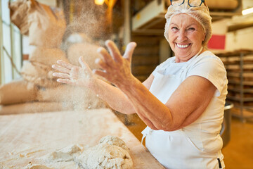 Woman as a baker claps flour from hands in bakery