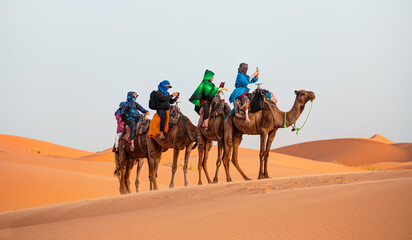 Tourists on safari - Caravan of camel in the sahara desert of Morocco at sunset time