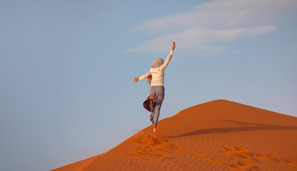 Muslim woman in gray trousers and a scarf jumps on the sands of the Sahara desert - Sahara, Morocco 