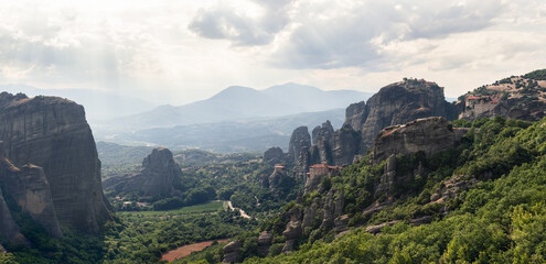 Aerial panoramic view over spectacular Thessaly plain landscape and byzantine monasteries of Meteora perched on sheer rocks, rays of the evening sun penetrate thick white clouds, Greece