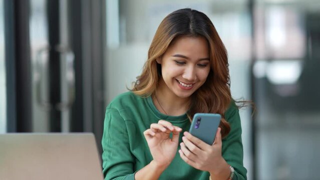 Young Asian women are enjoying using smartphone and social media application with pleasure and pleasure at the office.