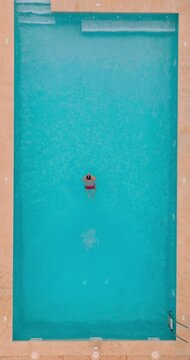 Vertical video. Aerial view as a man dives into the pool and swims. Slow motion