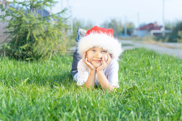 Fototapeta premium A child in a New Year's santa claus hat poses on the lawn
