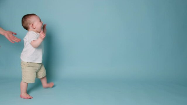 Happy toddler baby learns to walk and takes his first steps. Child boy walks for the first time on a studio blue background. Kid age one year