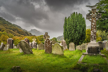 Ancient graves with Celtic crosses in Glendalough Cemetery with mountains and dramatic storm sky in...
