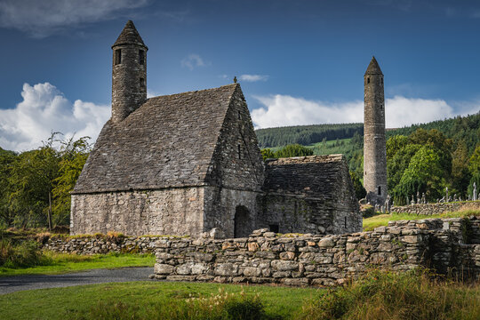 Medieval church, ancient graves, Celtic crosses in Glendalough Cemetery with forest and mountains in the background, Wicklow, Ireland