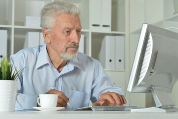 Elderly man sits with a computer in the office