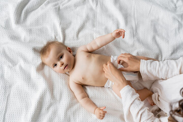 Top view of parent changing diaper on infant daughter on bed at home. - obrazy, fototapety, plakaty
