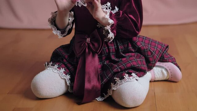 Cute little girl in an vintage burgundy dress is playing with a hair clip. The concept of children theater productions and developing acting circles. Pink background