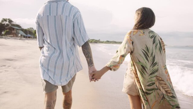 Rear view of young couple holding hands while walking at the beach