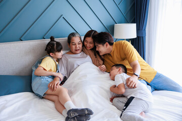 Fototapeta premium Happy family, Parent and children visit grandmom in bedroom, sitting together on bed, hug, smile at home.