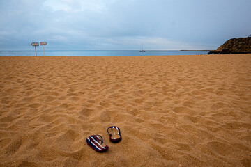Abufara beach in the moring with striped flip flops and sail boat