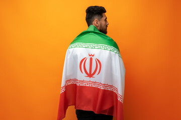 Fototapeta premium Portrait of a young casual man holding flag of Iran against orange background
