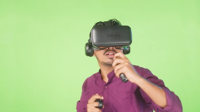 Excited young man with vr or virtual reality headset playing video game on metaverse using joystick on green screen background - concept of technology, entertainment and imagination
