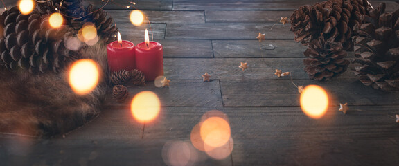 Two burning candles for christmas, dekorated on dark wood with fairy light and pine cone....