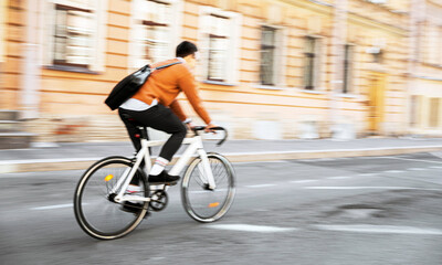Fototapeta na wymiar Blurry photo. Urban transport. A cyclist goes to work with a briefcase. .