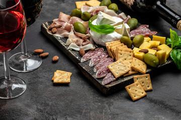 Antipasto board with sliced meat, ham, salami, cheese, olives and wine on a dark background