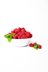 Fresh organic raspberries in a white bowl with a bit of mint isolated on white background with copy space.Vertical photo