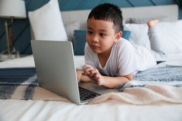 Asian kid boy using laptop study online with video call teacher at bedroom for distant learning.