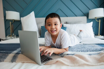 Asian kid boy using laptop study online with video call teacher at bedroom for distant learning.