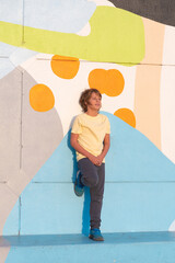 Boy enjoys with his mobile phone doing activities, multicoloured wall background, blond nilo smiles looking at his mobile phone.