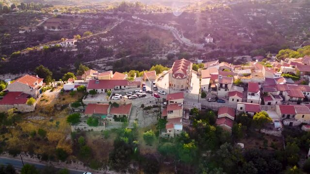 Aerial drone sunset footage of traditional countryside hilltop village Vouni, in Limassol, Cyprus. 360 view of christian church Ioannis Prodromos, ceramic tiled roof houses, narrow streets from above.