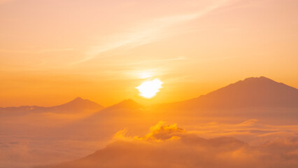 Fototapeta na wymiar Golden sunrise over white puffy clouds with distant mountains on horizon