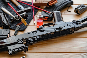 Black disassembled shotgun and cleaning tools on wooden table .