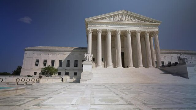 Turning wide angle view of facade of US Supreme Court building with Authority of Justice sculpture in front on a sunny summer day.