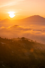 Golden sunrise over white puffy clouds with distant mountains on horizon. Sun ray through the mist in the mountains