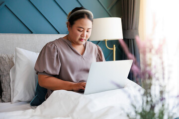 Asian woman working on laptop at home on the bed through internet for her business.