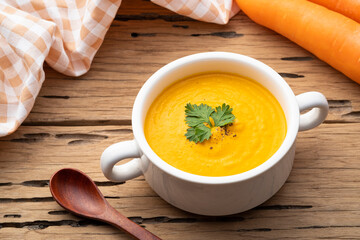 Bowl of tasty Creamy Carrot Soup with vegetables on wooden table,Healthy food