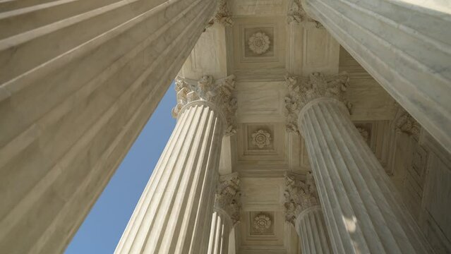 Slow motion looking up at the top of Corinthian columns in front of US Supreme Court in Washington, DC, showing power over people and business.