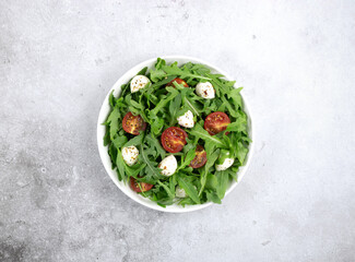 Green salad with arugula, cherry tomatoes, mozzarella cheese and olive oil on a gray background. View from above. 