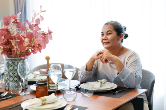 Smilling Asian Older Woman  Waiting Breakfast Food By Sitting At Dinning Table At Home.