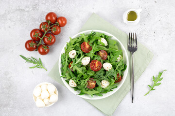 Low calorie green salad with arugula, cherry tomatoes, mozzarella balls on a gray background. View from above.