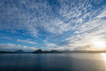 Fototapeta na wymiar 青空と流れゆく白い雲と朝日を映す洞爺湖面