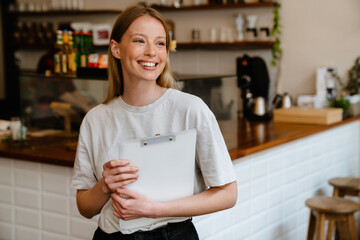 Blonde white woman smiling and holding clipboard while working in cafe