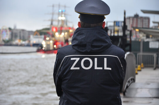 Der Zollbeamte im Hamburger Hafen: in Uniform am Wasser mit Schiffen im Hintergrund.