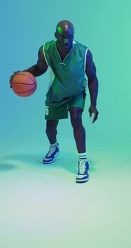 Vertical video of african american male basketball player bouncing ball on green background