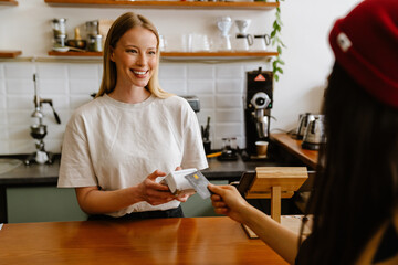 Blonde white barista woman working with terminal in cafe