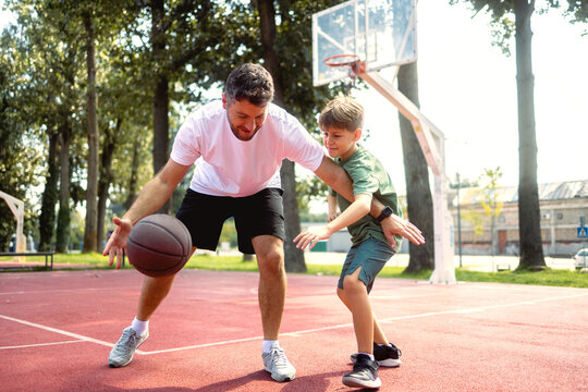 Father and son at public basketball court playing basketball.