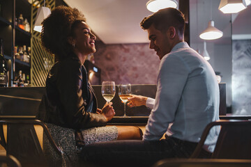 Romantic couple on a date talking holding a glass of white wine sitting at the bar counter in the night - Powered by Adobe