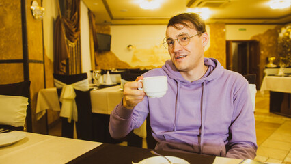 Fototapeta na wymiar Young man in glasses drinking coffee, talking to unknown person sitting in restaurant.