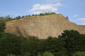 Mountain with surface mining behind green trees, blue spring sky, concept: nature, industrial (horizontal), Pfeffelbach, Kusel, RLP, Germany