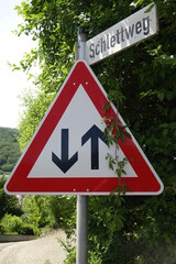 Red, white and black German traffic sign 125 'Gegenverkehr' (oncoming traffic) with road name on top, sunny spring day, concept: attention, regard (vertical), Wolfstein, RLP, Germany