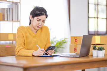 Business Asian women working on laptop computer checking customer order online shipping box at home. Starting Small business entrepreneur SME freelance. Online business, Work at home SME concept.