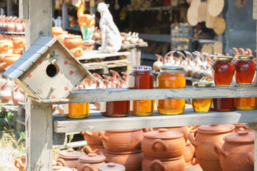 Street market in Georgia. Clay pots and other products are on display in the background, and glass jars of honey are in the foreground.