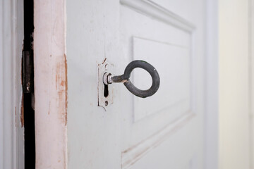Close-up of a vintage large key inserted into the keyhole of a white wooden door.